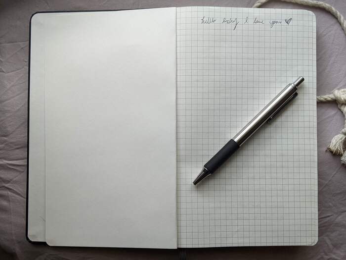 page of a notebook with pen resting on top. single line of text: 'hello baby i love you'