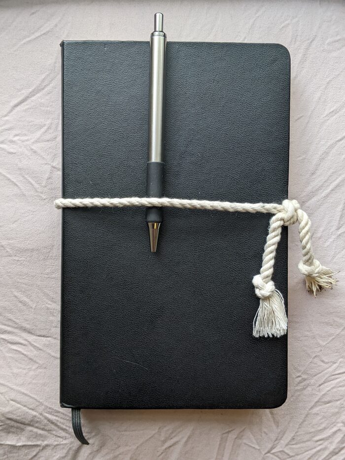 closed notebook with a pen on the cover, bound closed by rope